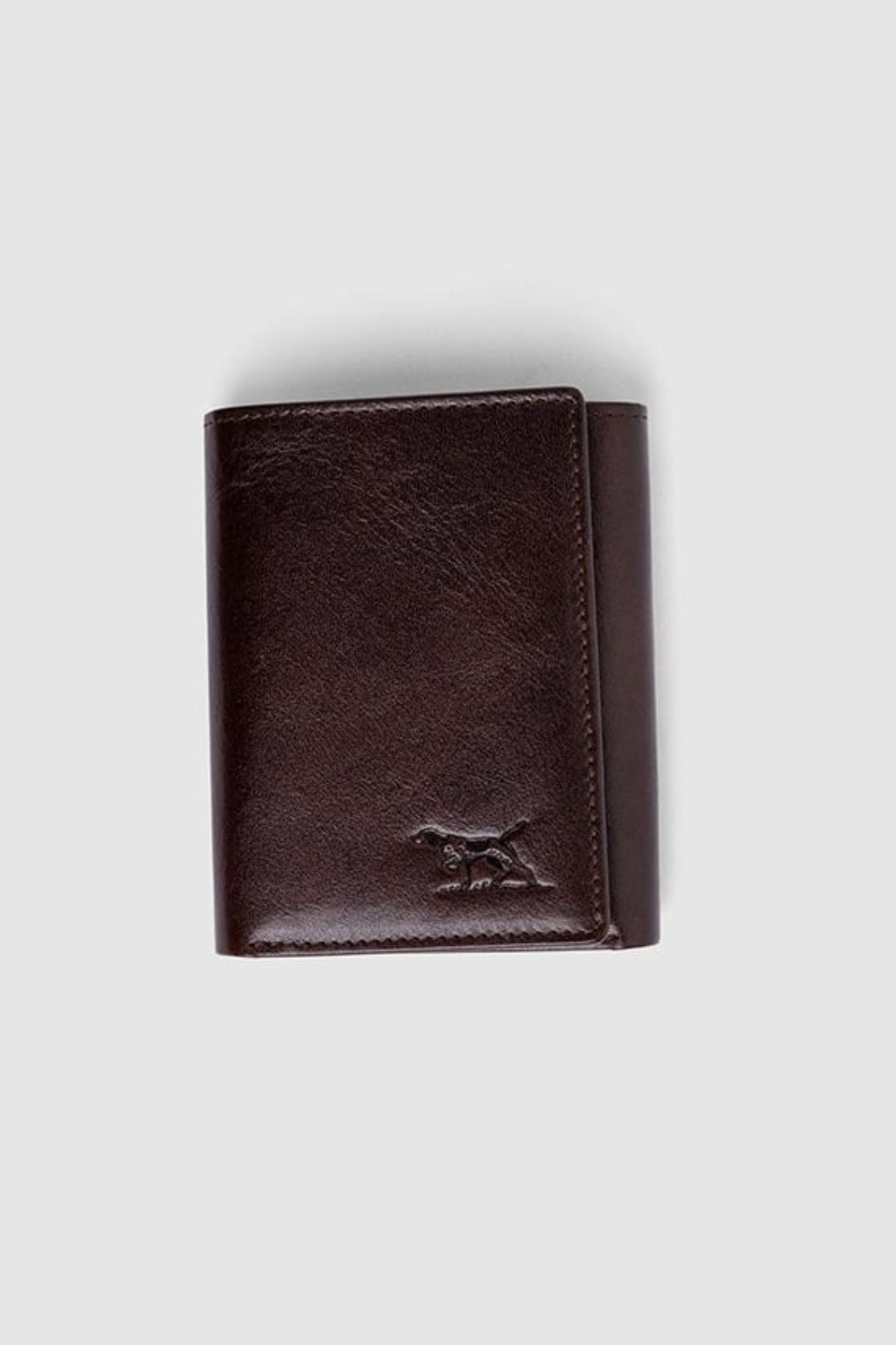 The Rodd & Gunn Westport Tri Fold Wallet, crafted from dark brown Italian leather with RFID protection and a subtle dog logo embossed in the bottom right corner, is photographed on a plain light gray background.