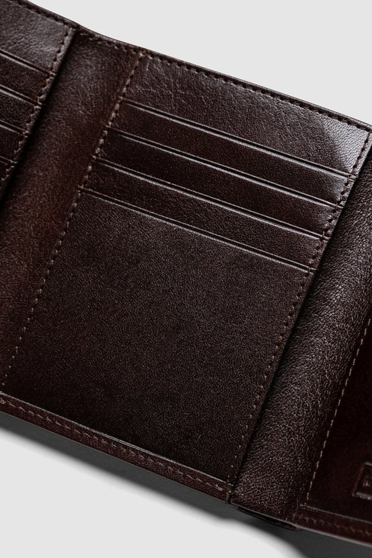 Close-up of the Rodd & Gunn Westport Tri Fold Wallet in dark brown Italian leather, featuring multiple card slots, textured material, and RFID protection. Shown open and empty against a light gray background.