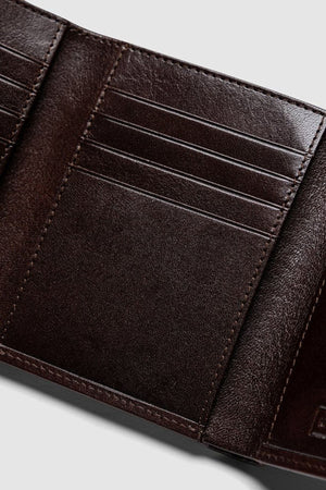 Close-up of the Rodd & Gunn Westport Tri Fold Wallet in dark brown Italian leather, featuring multiple card slots, textured material, and RFID protection. Shown open and empty against a light gray background.