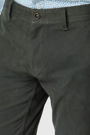 Close-up of a person wearing Rodd & Gunn Thomas Road 2.0 Chino Pant in dark green Italian-woven fabric, featuring a button and zipper, paired with a blue patterned shirt tucked at the waistband.