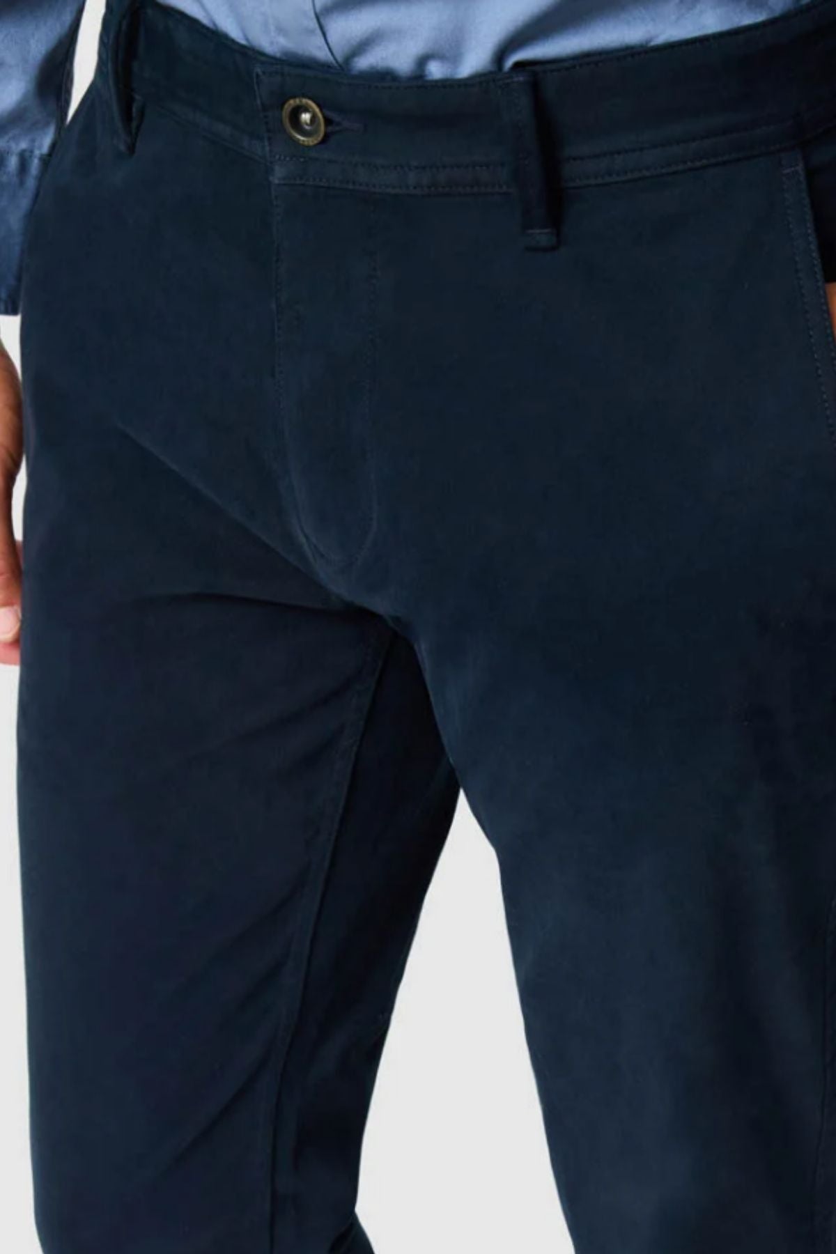 A close-up of a person wearing Rodd & Gunn Thomas Road 2.0 Chino Pant in dark navy blue Italian-woven fabric and a light blue shirt, highlighting the custom fit, button closure, waistband, fly, and front pockets.
