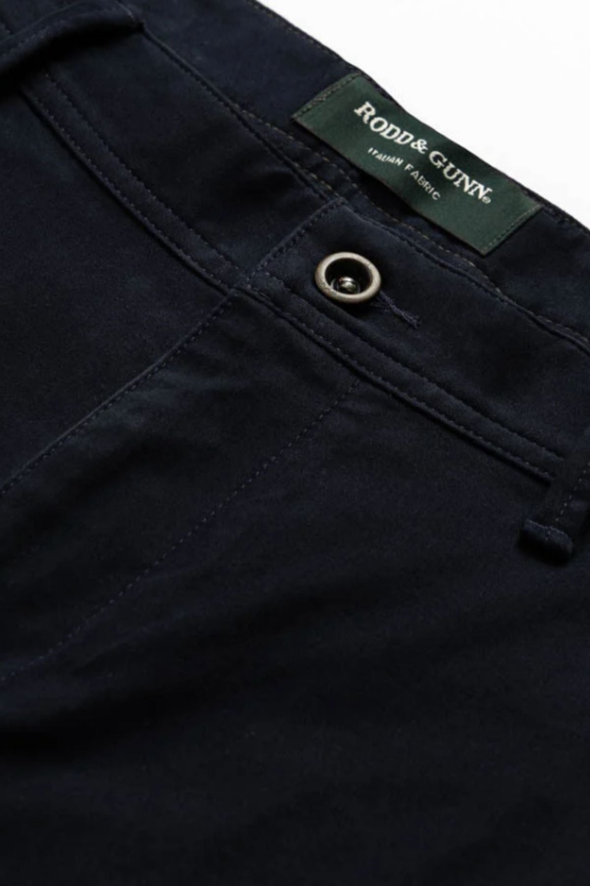 Close-up of the waistband and upper front of the Rodd & Gunn Thomas Road 2.0 Chino Pant in dark navy, featuring a metal button and a green Rodd & Gunn label stitched inside.