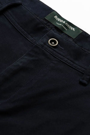 Close-up of the waistband and upper front of the Rodd & Gunn Thomas Road 2.0 Chino Pant in dark navy, featuring a metal button and a green Rodd & Gunn label stitched inside.