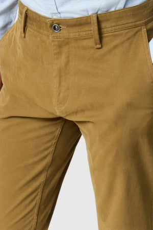 Close-up of a person wearing Rodd & Gunn Thomas Road 2.0 Chino Pant in tan, paired with a light blue checkered shirt tucked in. Only the waist and upper legs are visible; hands rest casually in their pockets.