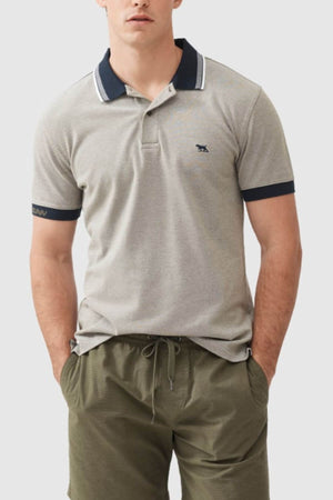A person wears the Rodd & Gunn Masterton Sports Fit Polo in modern slim fit and light gray, made from premium USA cotton, with a dark blue collar and light brown trim. A small dark logo adorns the chest. They stand with hands in olive green shorts' pockets against a neutral background.