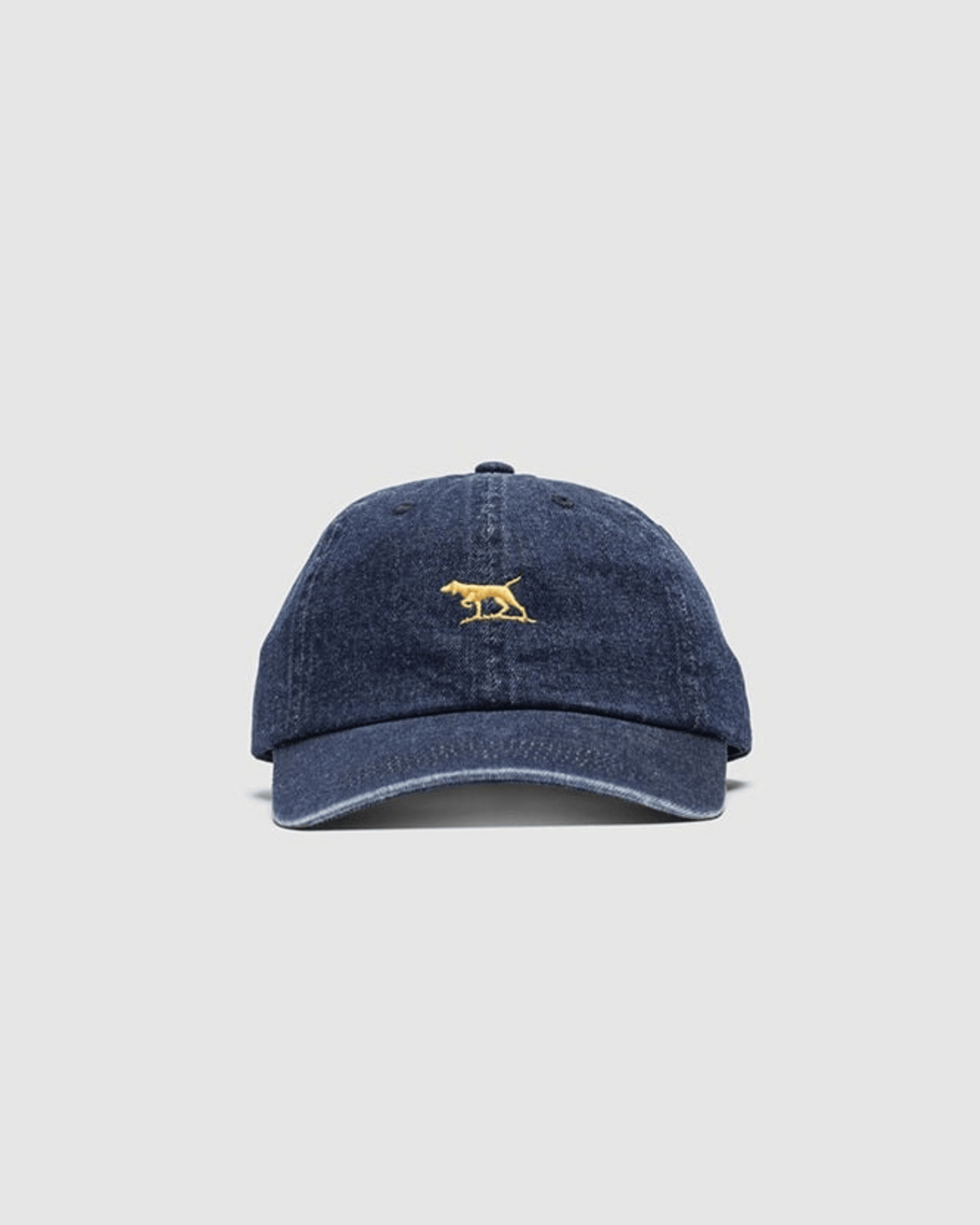 The Rodd & Gunn Gunn Cap in blue denim is made from heavy-duty cotton twill and features a small yellow embroidered animal on the front, set against a plain light gray background.