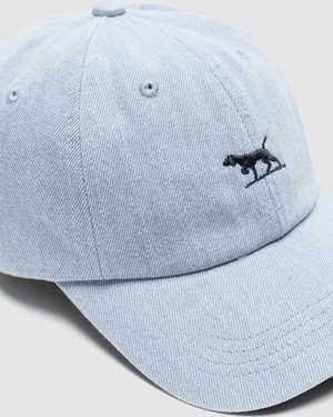 The Rodd & Gunn Gunn Cap is made from heavy duty cotton twill in light blue denim and features a small black embroidered dog on the front.