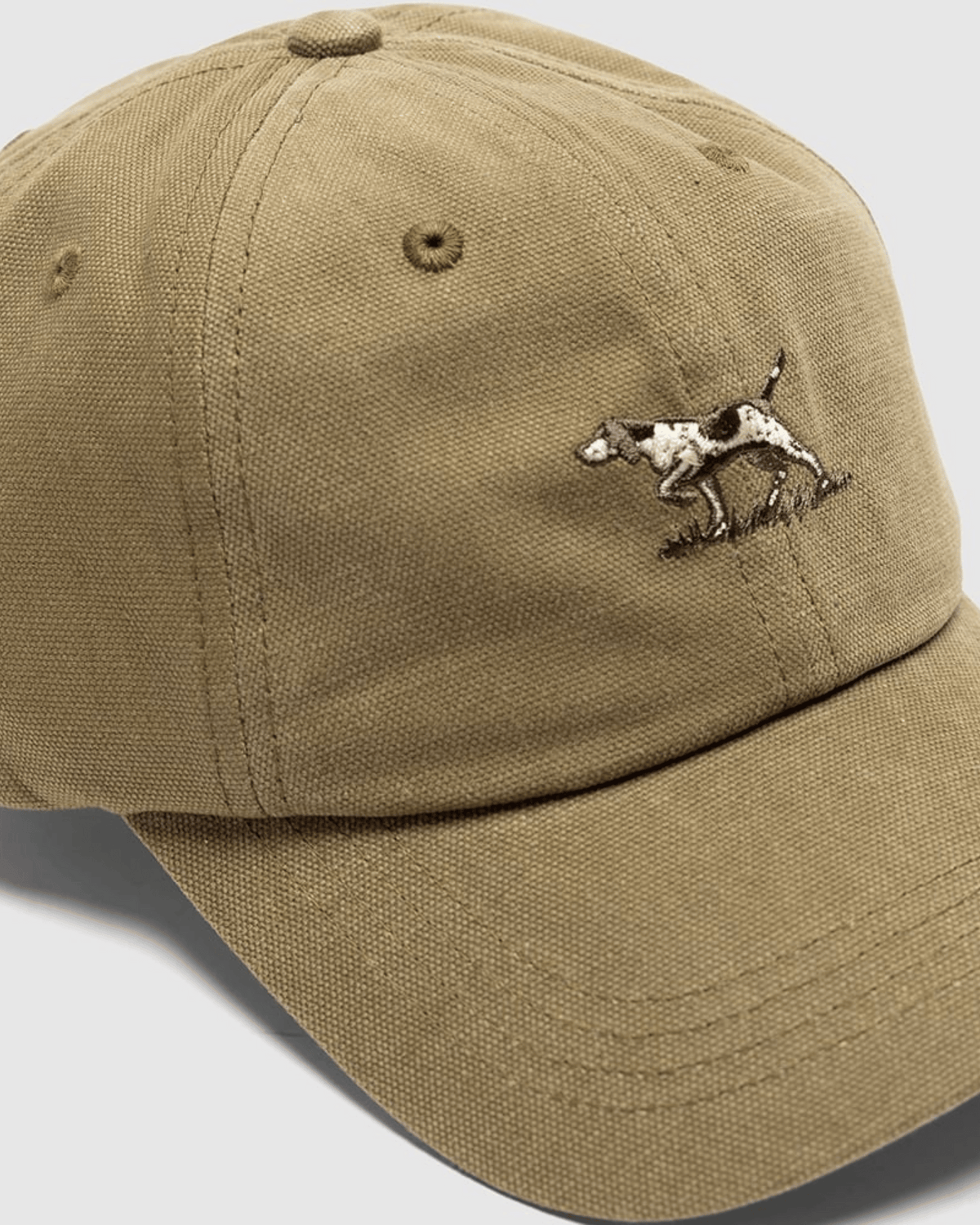 The Rodd & Gunn Signature Cap is a beige cotton twill baseball cap with ventilation holes, a curved brim, and an embroidered white and brown dog in a pointing stance on the front, combining style and comfort.