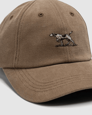 A close-up of the Rodd & Gunn Signature Cap in brown cotton twill, featuring embroidered artwork of a spotted dog standing on grass on the front panel.