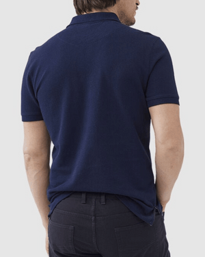 A man wearing the Rodd & Gunn The Gunn Polo made from comfortable, navy blue Australian cotton and dark pants is shown from the back. The shirt features short sleeves, a collar, and the man is standing with his arms relaxed at his sides against a neutral background.