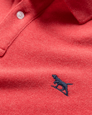 Close-up of the Rodd & Gunn The Gunn Polo, a modern fit red textured shirt made from soft Australian cotton, with a white button and a small navy blue embroidered dog logo on the chest.
