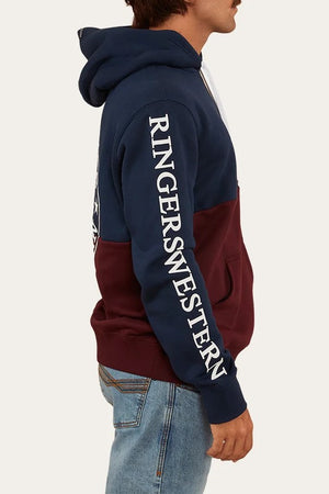 A person in blue and maroon Ringers Western Hahndorf Hoodie with "RINGERS WESTERN" in white on the sleeve, brushed fleece finish, and kangaroo pocket, paired with blue jeans, stands in profile against a plain background.