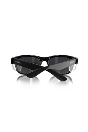 The SafeStyle Classics Black Frame Polarised Lens sunglasses, featuring a sleek design and subtle logo on the temples, sit on a reflective white surface. They offer excellent UV protection with their folded arms and polarised lenses.