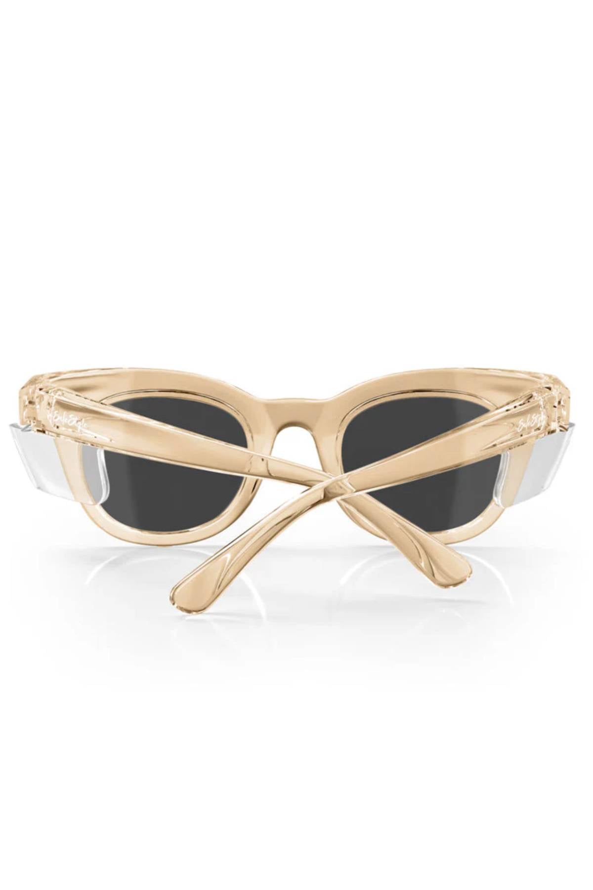 The SafeStyle Harps sunglasses boast a chic champagne frame with polarised dark lenses offering UV protection. Seen from the front, their crossed arms rest elegantly on a reflective white surface.