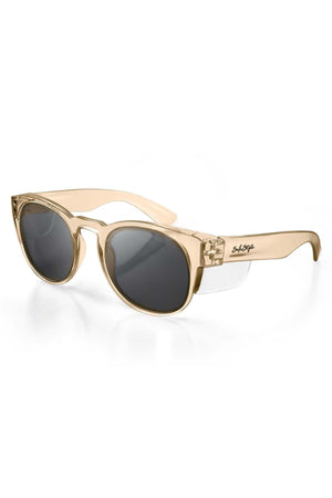 SafeStyle Cruisers Champagne Frame Tinted Lens sunglasses feature a thick beige translucent frame, dark oval polycarbonate lenses with UV400 protection, and a black logo on the left temple arm. Displayed on a white background.