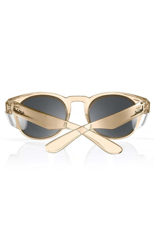 The SafeStyle Cruisers Champagne Frame Tinted Lens sunglasses, featuring a beige oval shape, polycarbonate lenses with UV400 protection, are shown from behind with crossed arms and the brand logo visible on each arm.