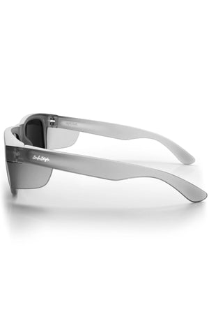 The Safestyle Fusions XL Matte Graphite sunglasses feature thick side arms, dark polarised lenses for UV protection, and "So Fetch" embossed in cursive on the left arm. Shown resting on a white surface from a side view.