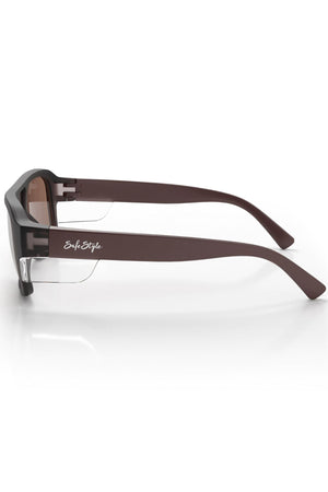 Side view of Safestyle Skylines with chocolate frame and brown polarised lens, featuring thick arms, clear side shields, and "SafeStyle" logo in white. These glasses offer UV400 protection and rest on a white surface.