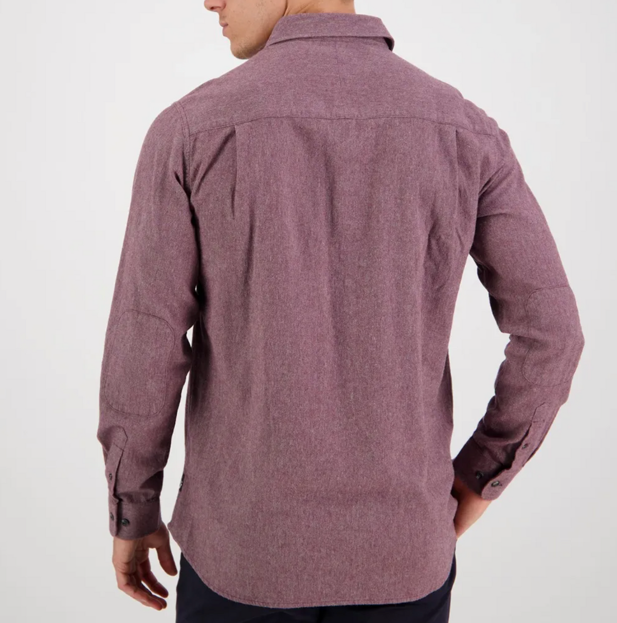 A man is seen from behind wearing the Swanndri Ranch Rd Shirt, a stylish maroon long-sleeve with a tailored fit, paired with dark pants. He stands against a plain white background, left hand on his hip and turned slightly to the left.