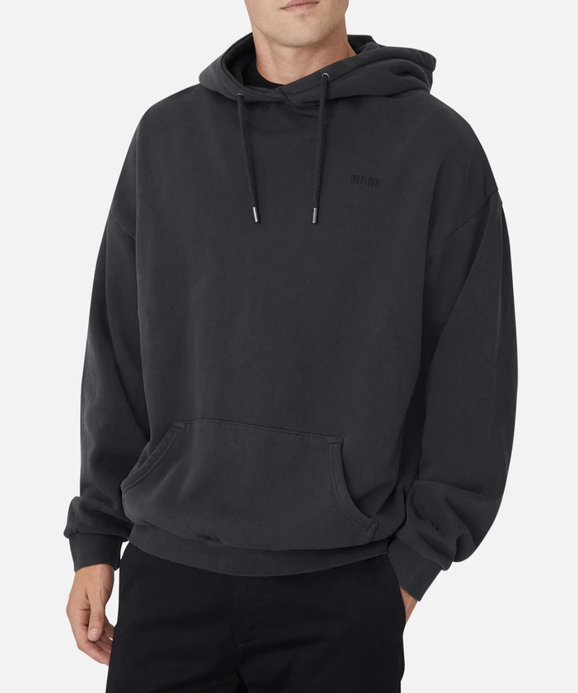 Someone wears the comfortable Industrie The Del Sur Hoodie in dark gray with an embroidered logo and drawstrings, paired with black pants against a white background. The face is partially obscured, highlighting the oversized fit and casual style of the outfit.