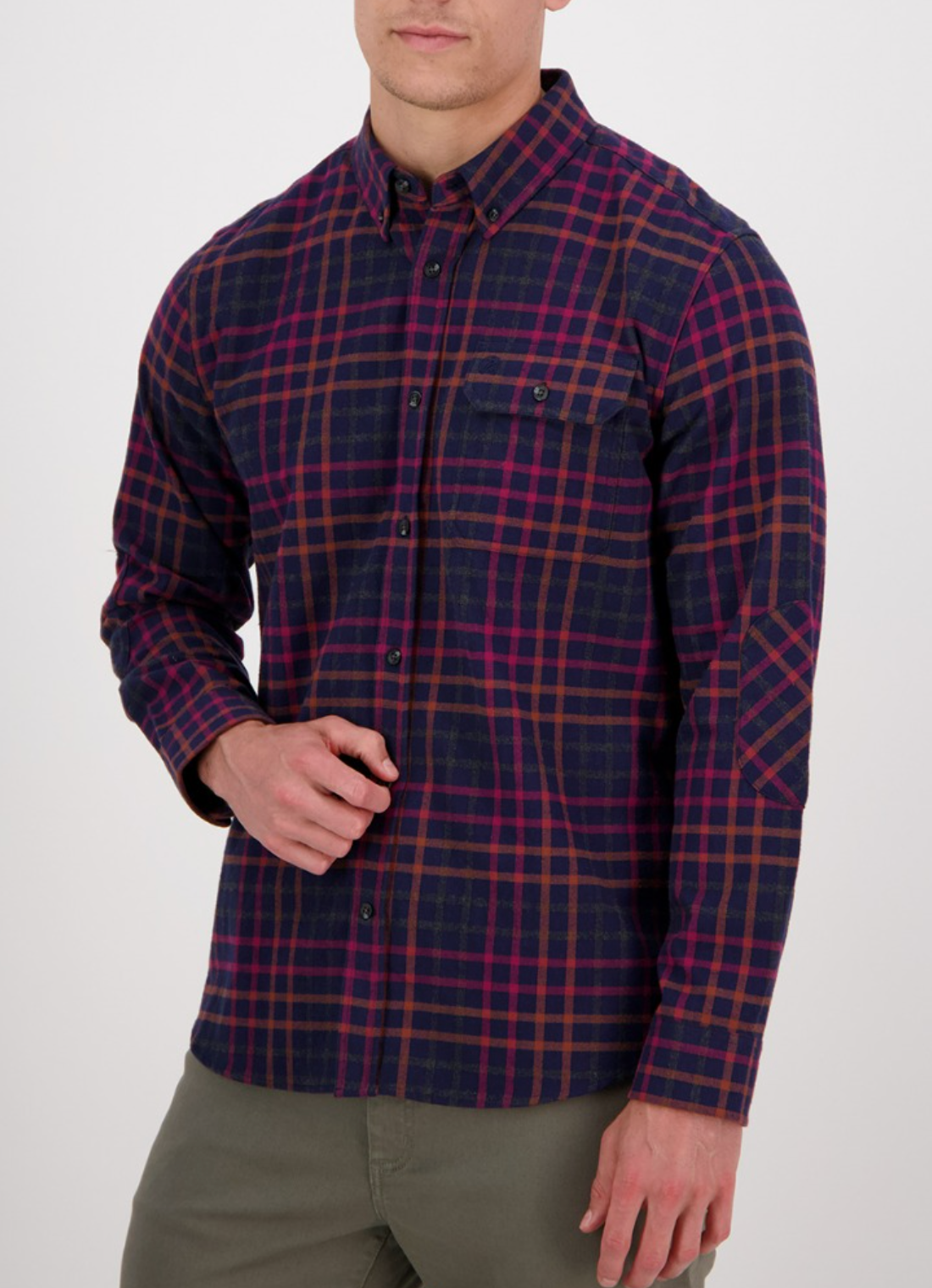 A man wears the Swanndri Eastcott Shirt—classic fit, long-sleeve, navy, red, and orange plaid in 100% cotton—paired with olive green pants, standing against a plain white background.