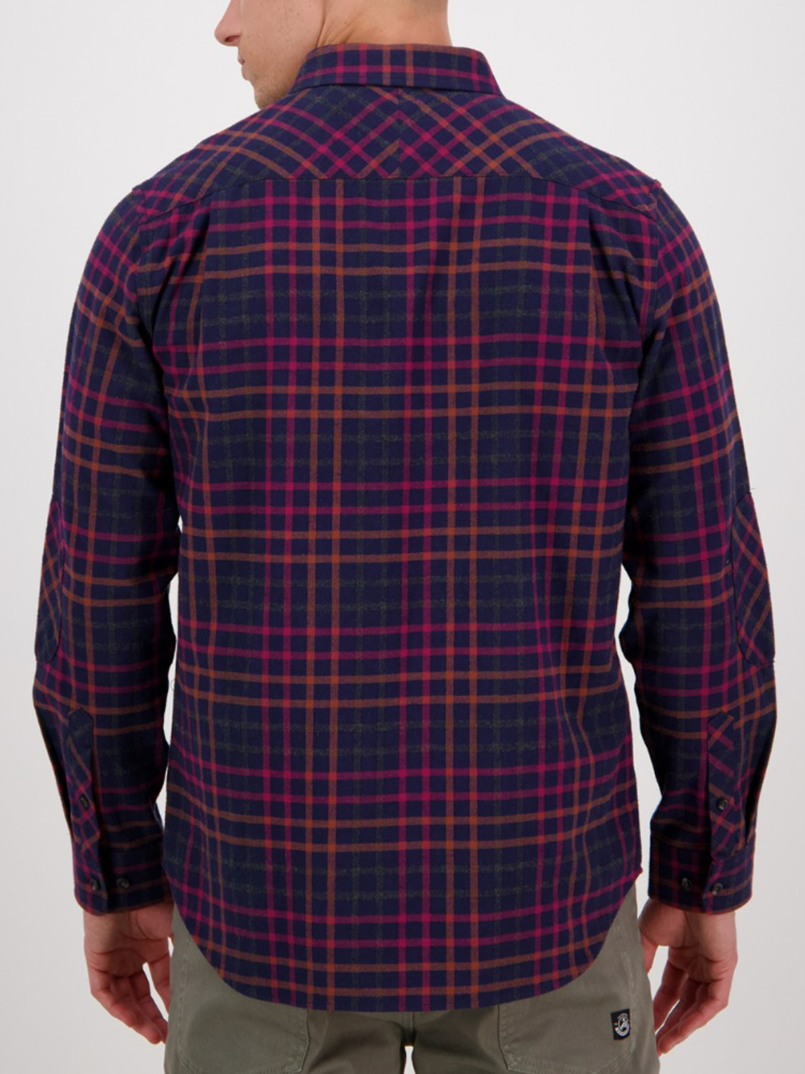 A man faces away from the camera wearing a Swanndri Eastcott Shirt, classic fit, 100% cotton with blue, red, and brown plaid lines, paired with olive green pants against a plain white background.