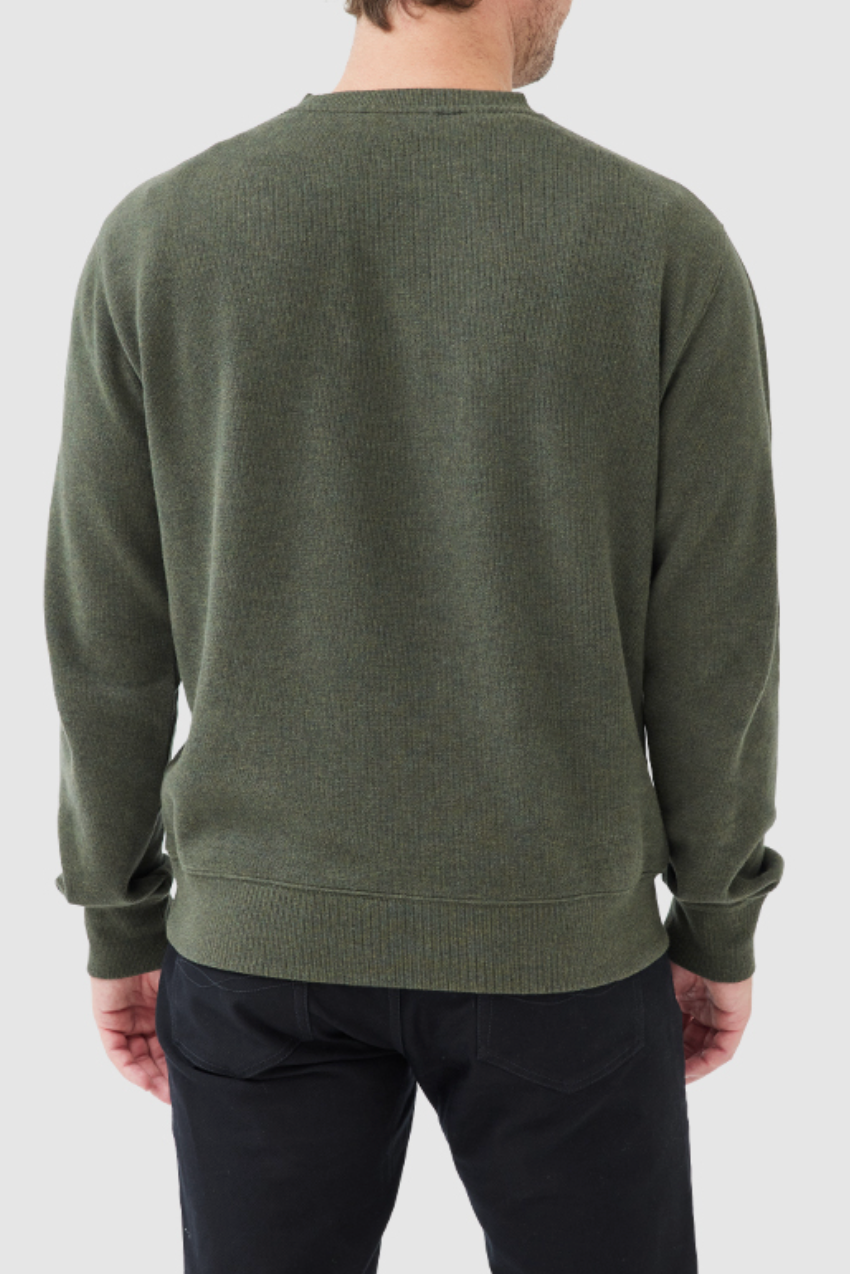 A person facing away from the camera is wearing a Rodd & Gunn Gunn Crew Neck Sweat in comfortable dark green, made of 100% cotton, paired with black pants. The background is light gray.