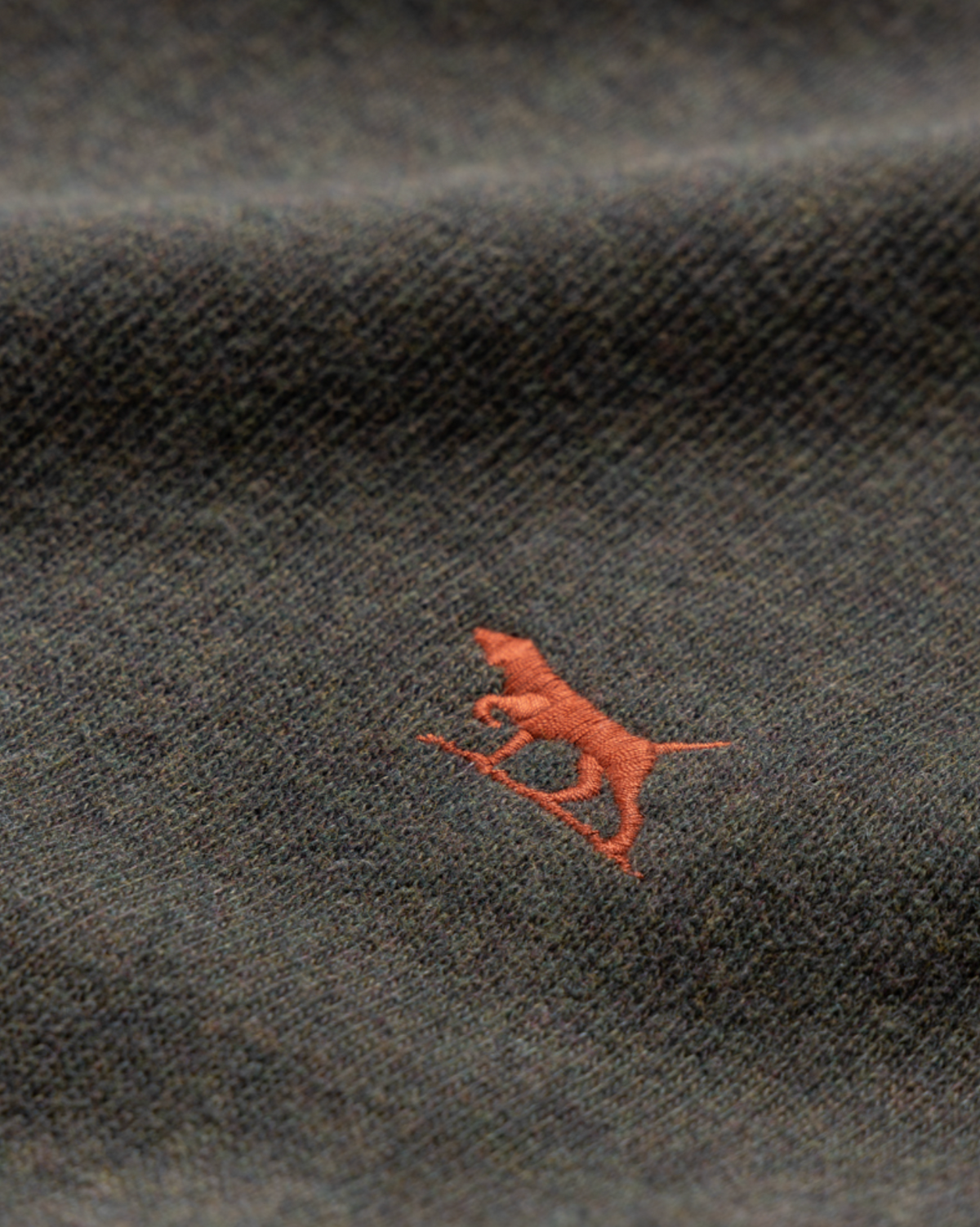 Close-up of a dark textured Rodd & Gunn Gunn Crew Neck Sweat, made from 100% cotton, featuring a small red embroidered logo of a dog on a surfboard.