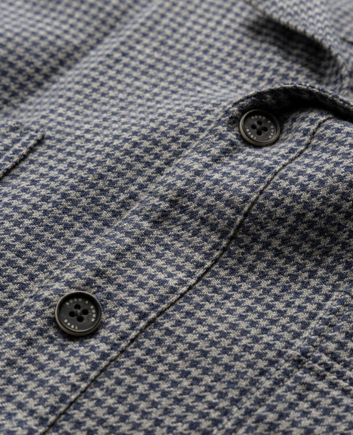 Close-up of the Rodd & Gunn Pentland Hills Shirt in 100% cotton, featuring a small gray and blue houndstooth pattern, two black buttons, and a visible pocket seam.