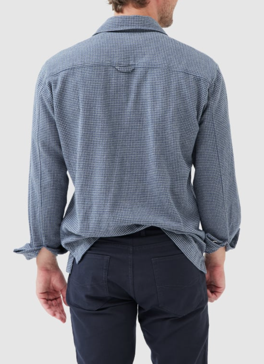 A person in a blue checked Rodd & Gunn Pentland Hills Shirt, made of 100% cotton, and dark pants stands with their back to the camera. Their right hand is relaxed by their side.