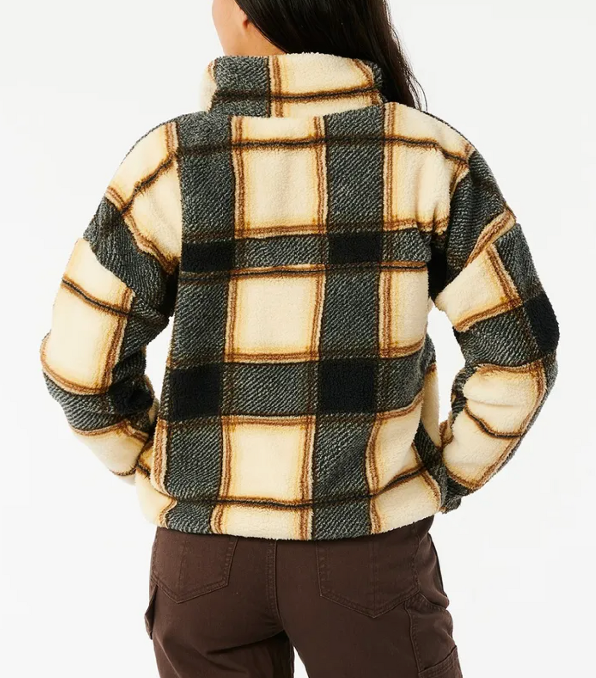 Person faces away, wearing the Rip Curl Kindred Palms Polar Fleece—a cozy, oversized cream, black, and tan jacket with bold plaid patterns and a high collar—paired with brown pants. Background is plain white.