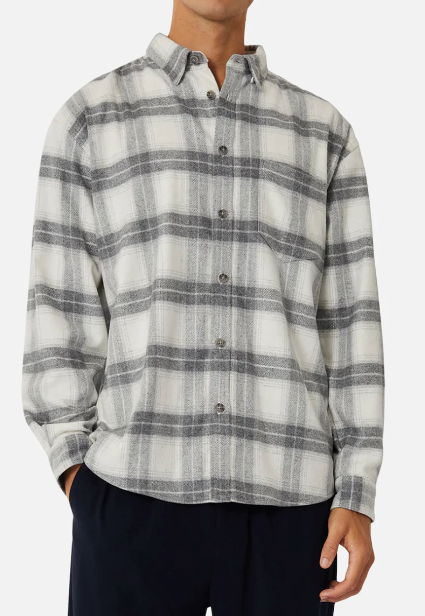 A person wearing the Industrie The Silverton Shirt in a stylish grey and white plaid, regular fit, long-sleeved with a crisp collar, pairs it with dark pants against a plain backdrop. With hands in pockets, their head is out of view.
