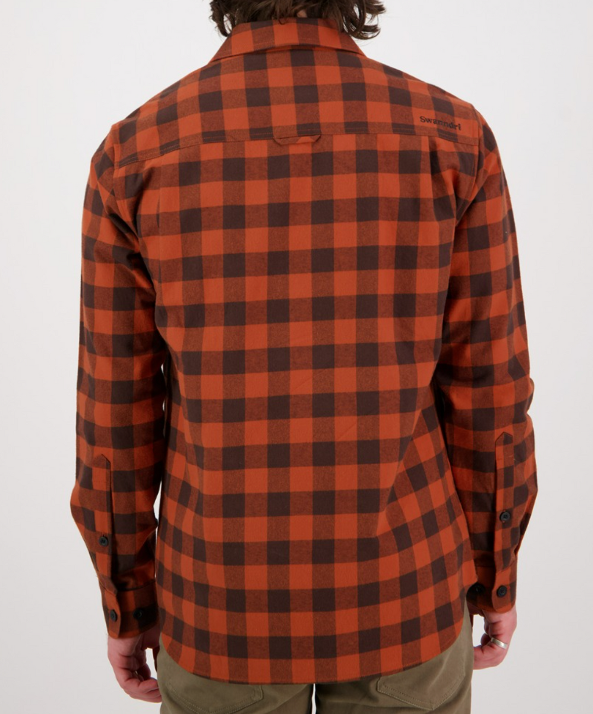 A person wearing the Swanndri Taranaki Tailor Shirt, a stylish, long-sleeved plaid in orange and dark brown made of 100% cotton, is shown from the back. Known for comfort and a visible logo on the upper right shoulder, it is paired with olive pants for a timeless look.