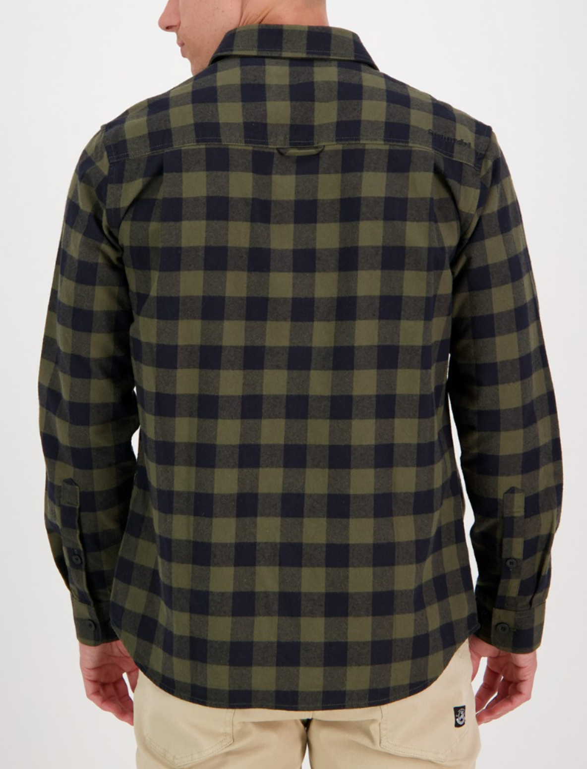 A person shown from the back wears the Swanndri Taranaki Tailor Shirt in green and black plaid (100% cotton, tailored fit, long sleeves) with beige pants against a plain white background.