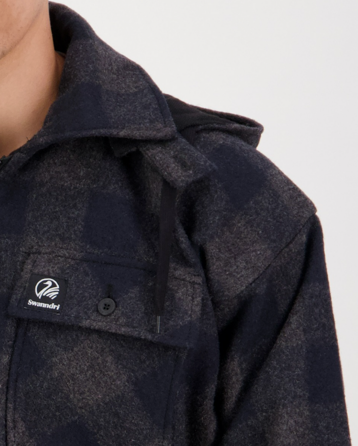 Close-up of a person wearing the Swanndri Mosgiel Zip Front Bush Shirt—a dark plaid 100% wool overshirt with a collar and chest pocket featuring the Swandri logo. Only the lower half of their face and shoulder are visible.
