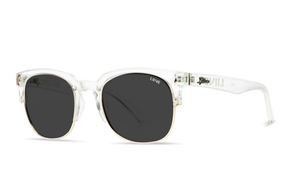 Liive Dylan Sunglasses feature clear polycarbonate frames and black round UV-protective lenses. "LIIVE" is labeled on the left lens, with subtle logo accents on the arms near the hinges. Displayed resting on a white surface.