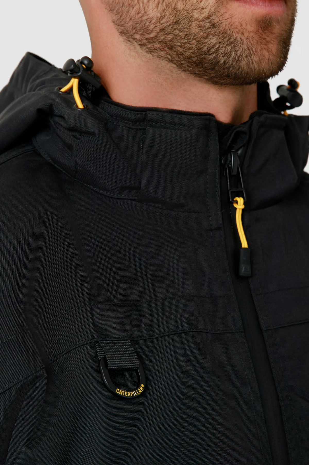 Close-up of a man's lower face and upper torso wearing the CAT Chinook Waterproof Jacket with yellow zipper pulls, adjustable hood, and a black tab labeled "Caterpillar.