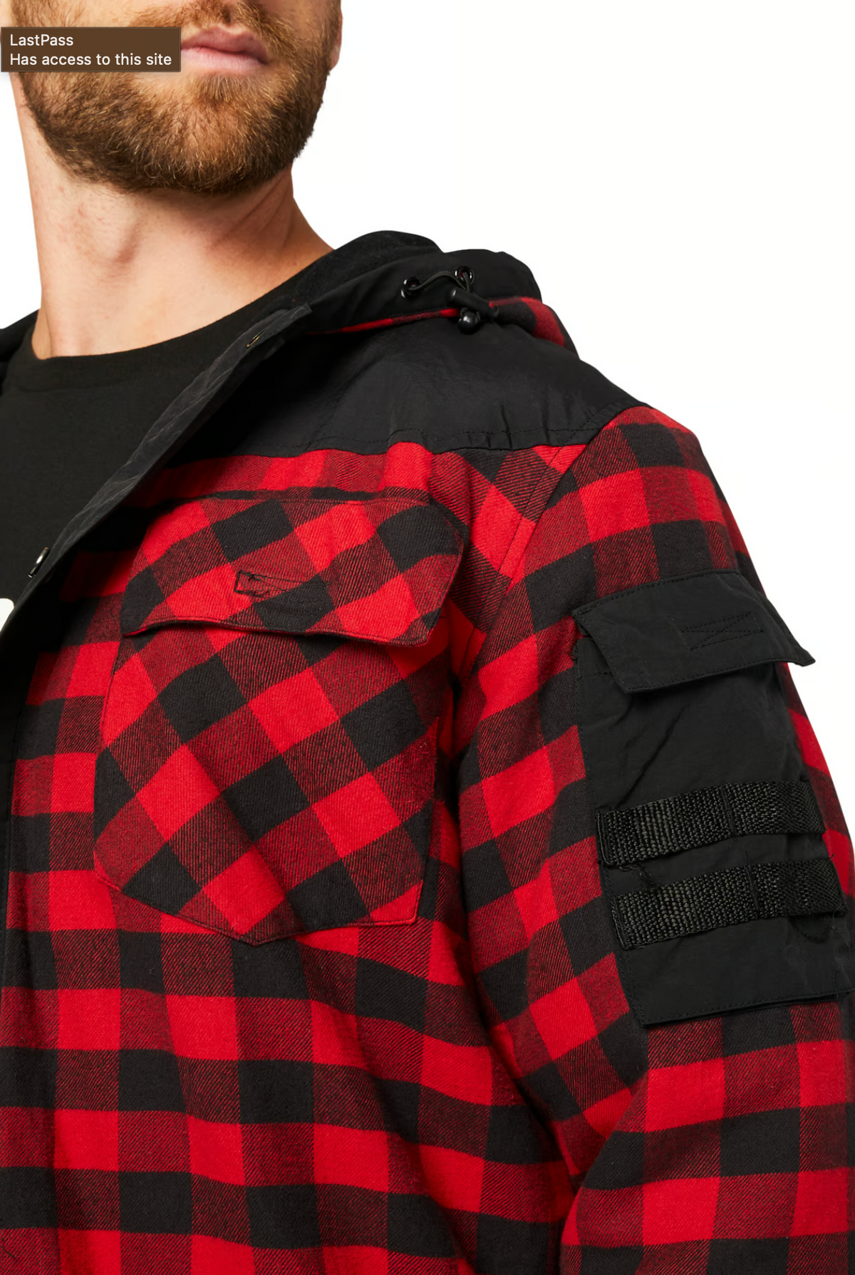 A person with a beard sports the CAT Sequoia Shirt Jacket, a red and black checkered cotton piece featuring buttoned chest pockets, fleece lining for warmth, and stylish black fabric arm patches. They wear a black hood and shirt underneath.