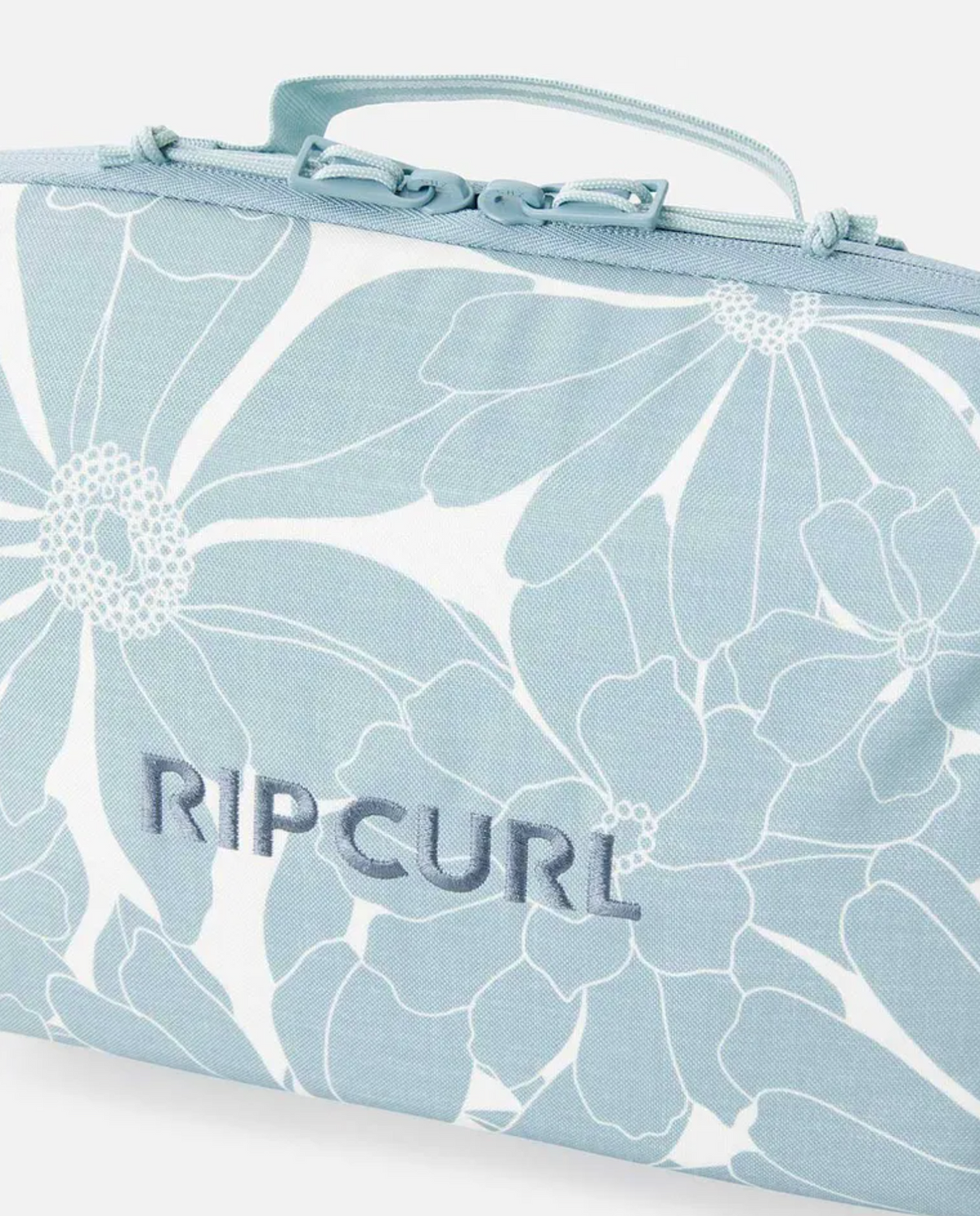 The Rip Curl Paradise F-Light Beauty Case is a light blue and white bag with a floral pattern, "RIPCURL" embroidered on the front, a top handle and zipper, and is made from recycled polyester.