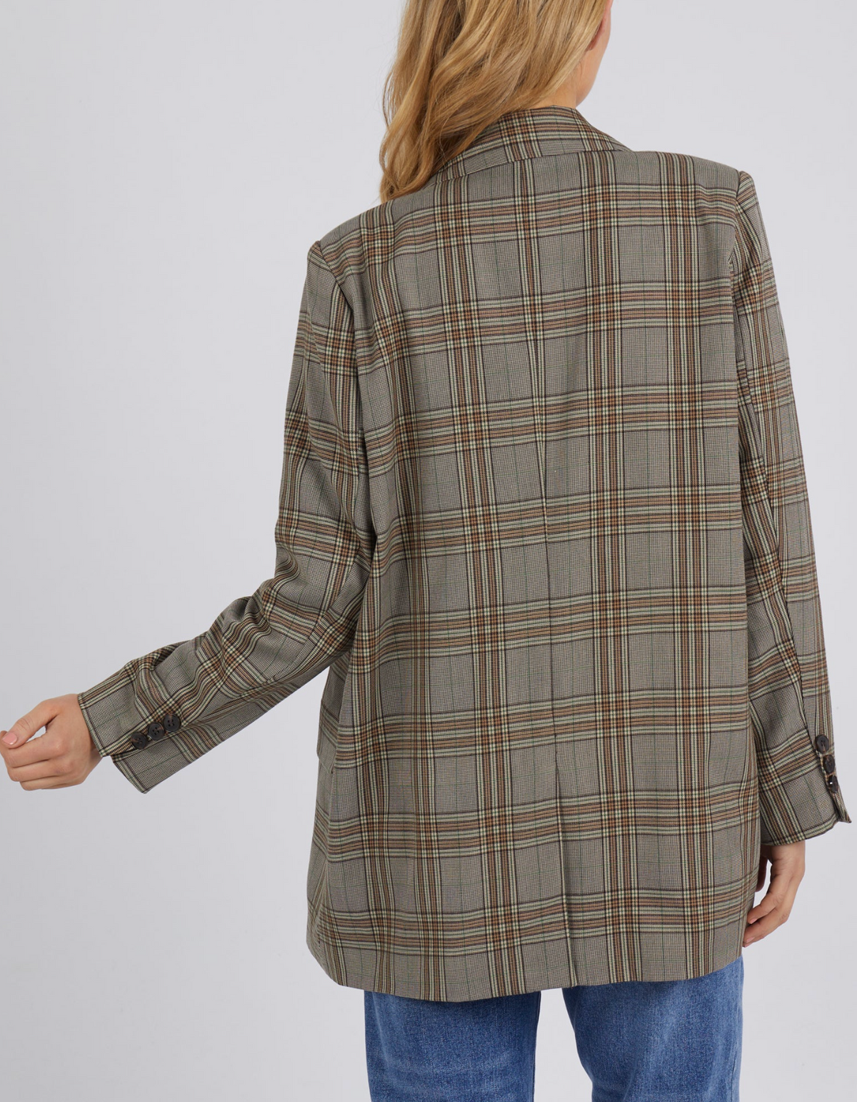 A person with long hair is seen from the back, wearing the oversized Foxwood Beatrix Blazer, a stylish brown and beige plaid design, paired with blue jeans. Their left hand is slightly extended.