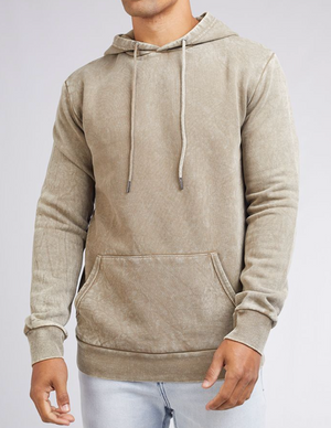 Someone wears a Silent Theory Hoody in light brown with a front pocket and drawstrings, set against a plain background. They're paired with light blue jeans, hands visible but face not shown.