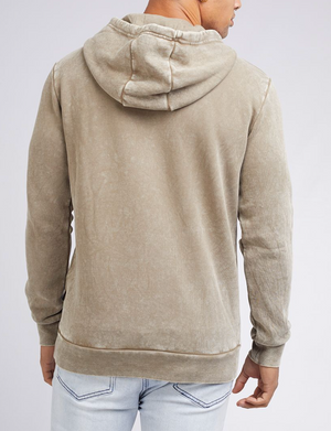 A person in a Silent Theory Hoody, light brown and comfortable, seen from the back with the hood down. They're paired with light blue jeans against a simple light background, exuding casual charm.