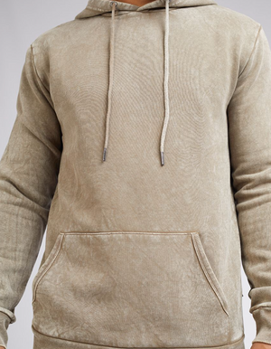 A person wears the Silent Theory Hoody, a comfortable light brown garment with a front pocket and drawstrings. Set against a neutral background, it has a textured, slightly worn look.