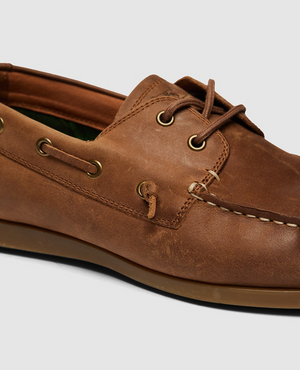 The Rodd & Gunn Gordons Bay Boat Shoe features a brown leather upper with visible stitching and laces. Gold eyelets provide contrast to the light brown rubber outsole, and the interior showcases a touch of green lining.