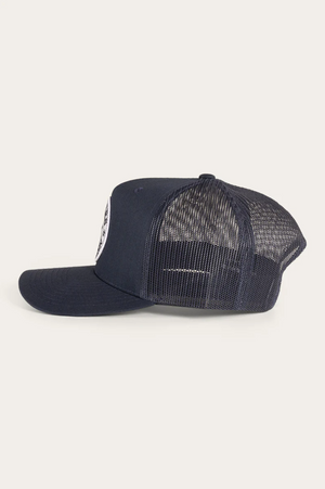 The Ringers Western Signature Bull Trucker Cap in navy blue features a solid cotton twill front, a black mesh back, and is shown from the side against a plain light background.