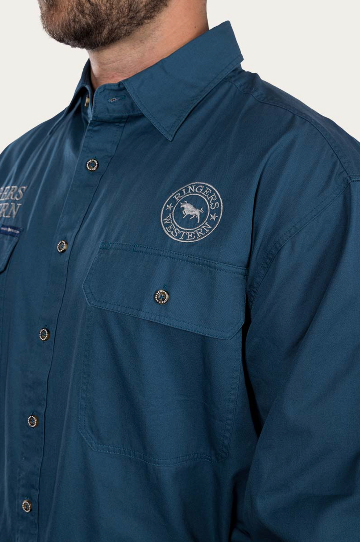 A person is wearing a blue Ringers Western Hawkeye Embroidered Shirt with UPF50+ protection, featuring the brand's logo on the chest pocket, complete with a collar and long sleeves against a white background.