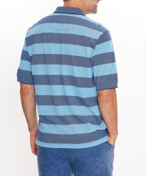 A man in a regular-fit Breakaway Syd Cotton Pique Polo, featuring blue and gray stripes, 100% cotton, stands with his back to the camera. He is wearing blue jeans and has short hair against a plain white background.