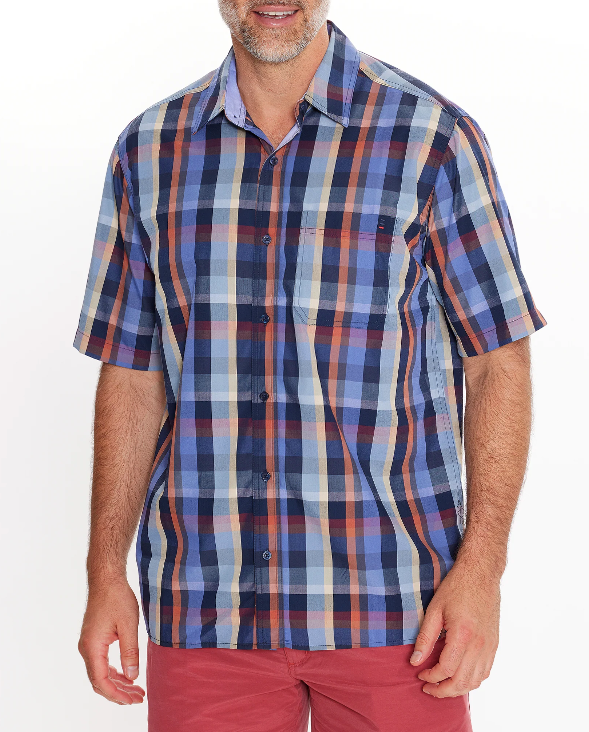 A man wears the Breakaway Rome Bamboo Blend Shirt, a comfy short-sleeved multicolored plaid button-up in shades of blue, red, and beige. He pairs it with red shorts against a plain white background.