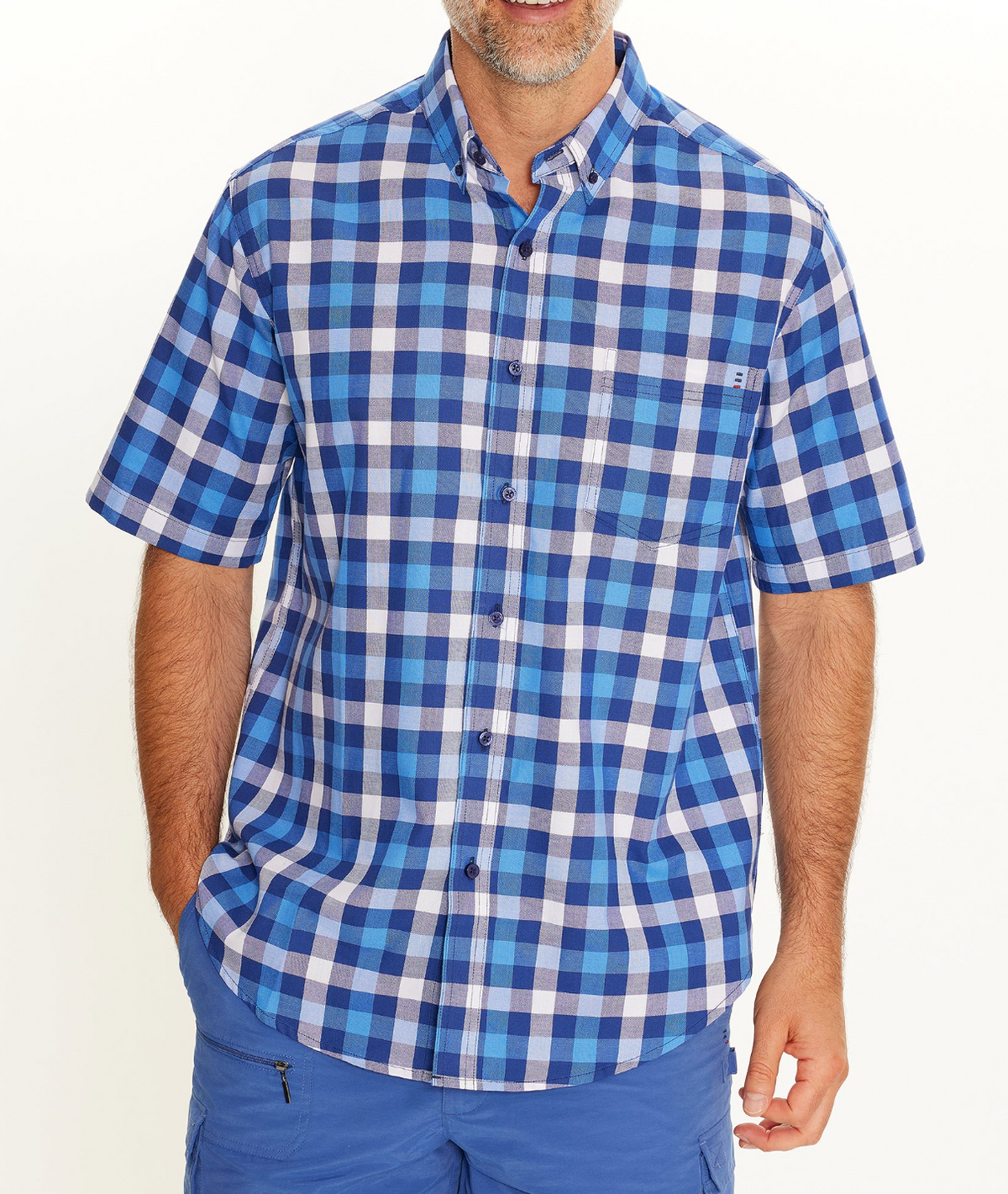 A man models the Breakaway Gil Oxford Shirt, a comfortable 100% cotton blue and white plaid casual shirt, paired with blue shorts against a plain white background. His face is mostly out of frame.