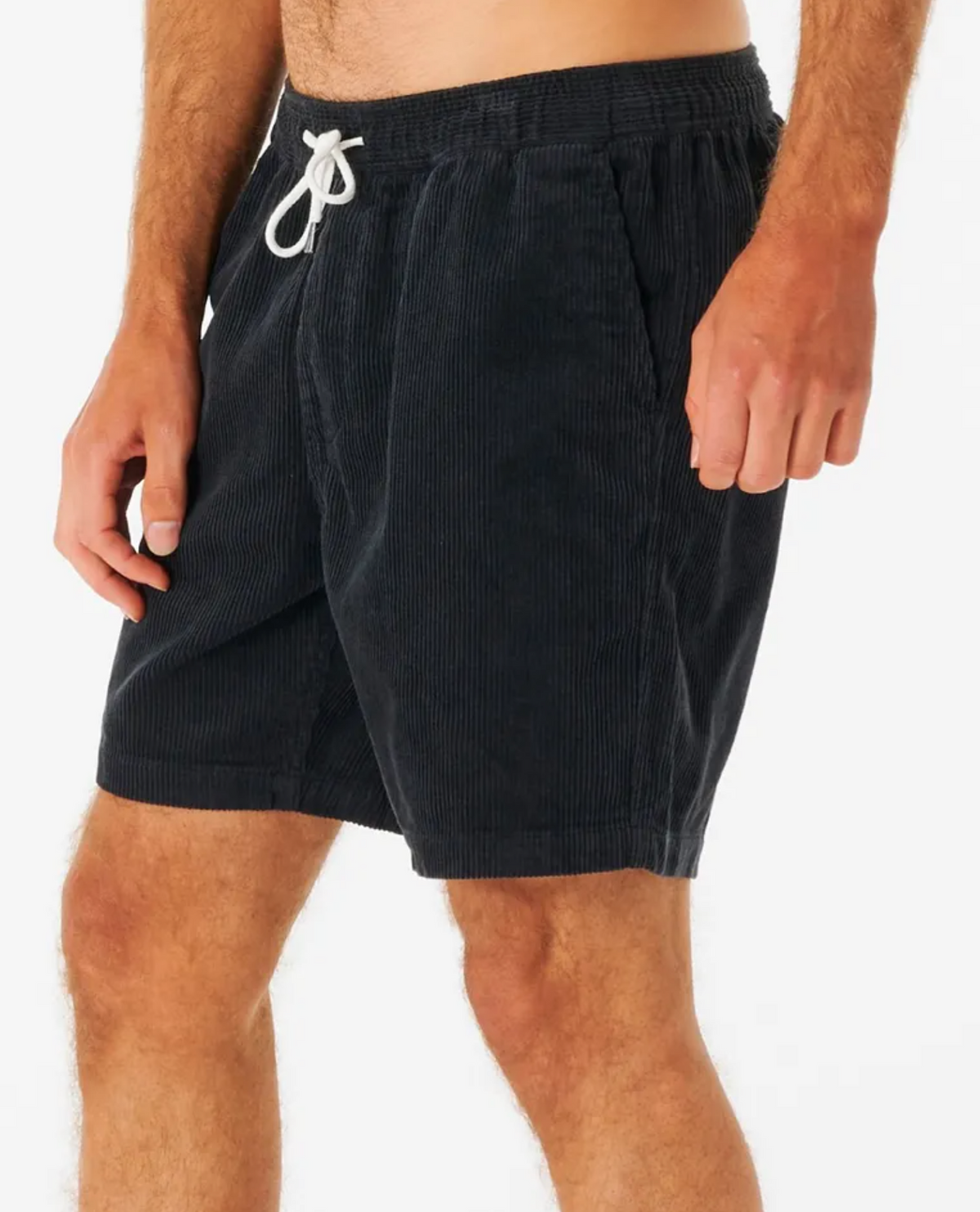 Wearing Rip Curl Surf Revival Cord Volley shorts, designed in navy blue with a classic 90s baggy fit, elastic waistband, and white drawstring, a person is posed relaxedly with one hand in a pocket against a plain white backdrop.